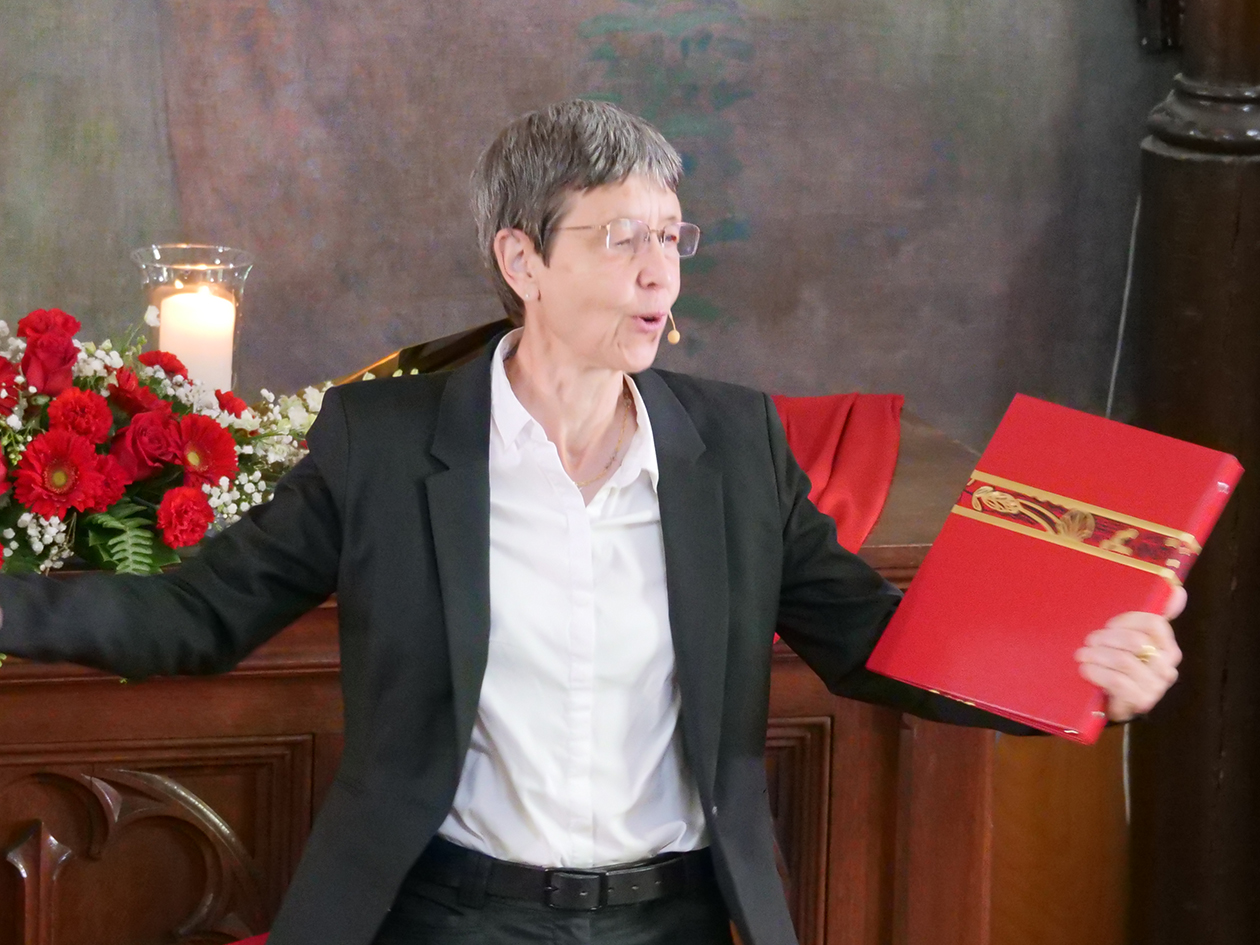 Pastor Daniela Mertz at the front of the church with a red book in her hand