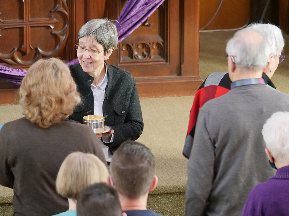 Pastor Daniela standing at the front of the church giving communion to members of the church