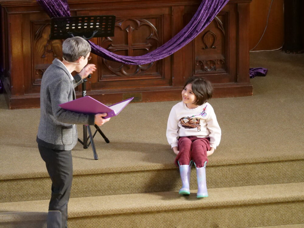 Sunday Worship service with Pastor Dani speaking to a small child on the alter