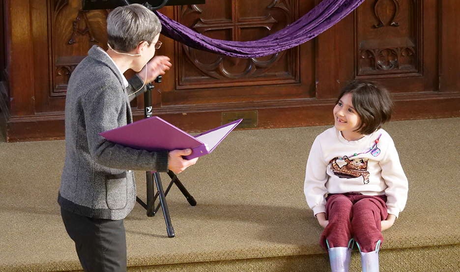 Pastor Dani standing and a young girl sitting on the step of the alter smiling.