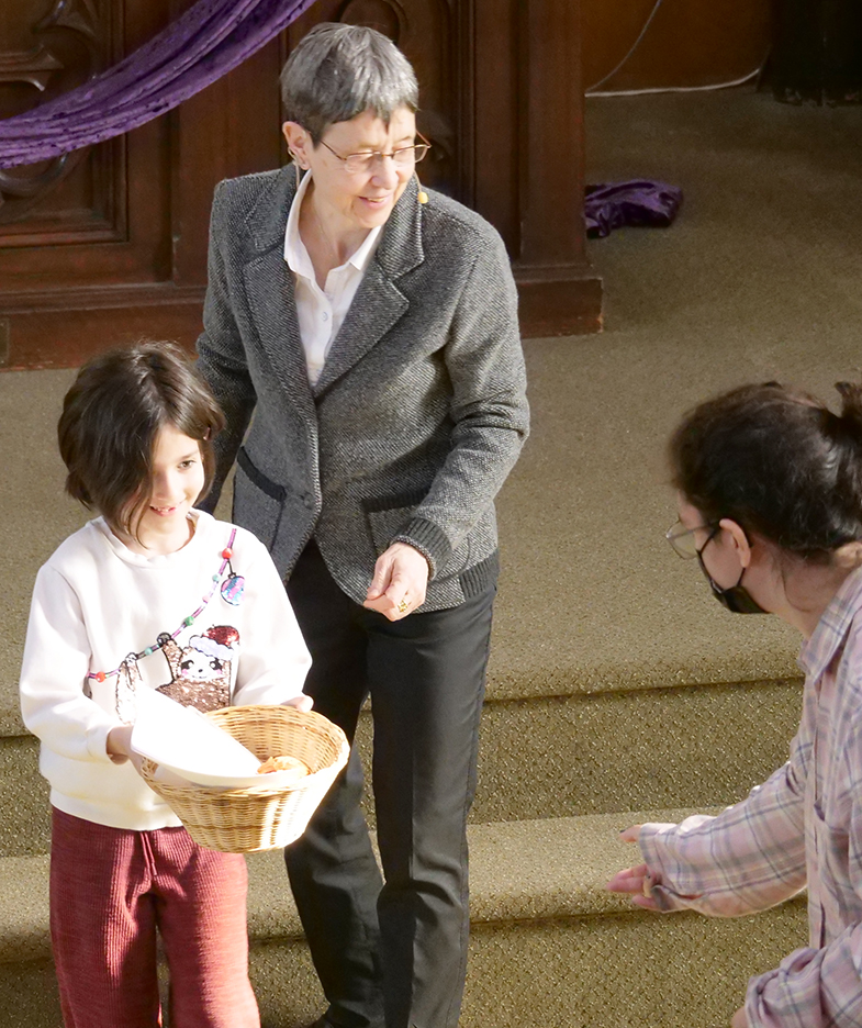 Pastor Dani smiling and young girl smiling while handing basket to a women