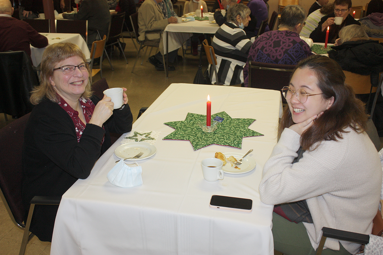 two women sitting across from each other drinking coffee and a red candle is lit in the middle of the table