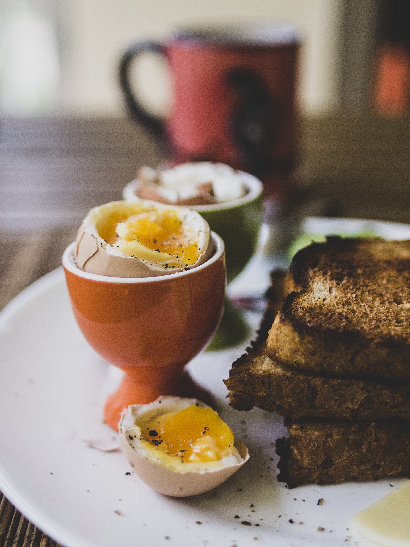 two eggs in egg cups beside a stack of toast