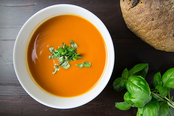 a photo of a white bowl of tomato soup with fresh basil on the top