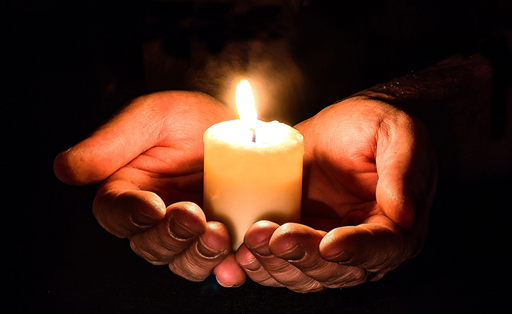 hands cupped and holding a lit small candle