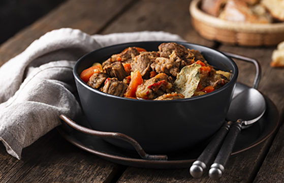 a bowl of stew on a table with a napkin and cutlery on either side